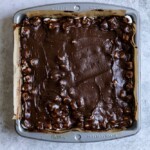 Chocolate frosting covering marshmallow brownies in a brownie pan.
