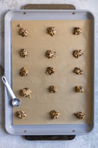 Mini chocolate chip cookie dough lined up on a sheet tray.