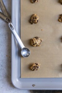 A closeup of mini chocolate chip cookie dough with a teaspoon next to it on a cookie sheet.