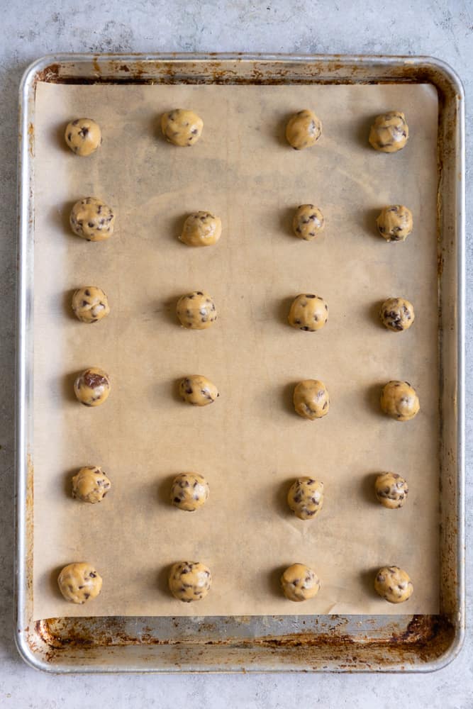 Cookie dough rolled into mini balls and lined up on a sheet tray.