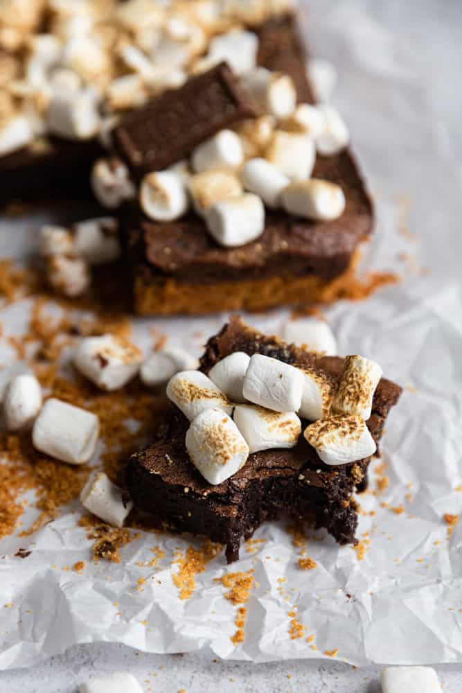 A S'mores brownie with a bite taken out on a piece of parchment paper.