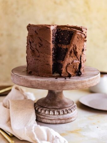 A chocolate cake with a slice cut out on an angle on a wooden cake stand.