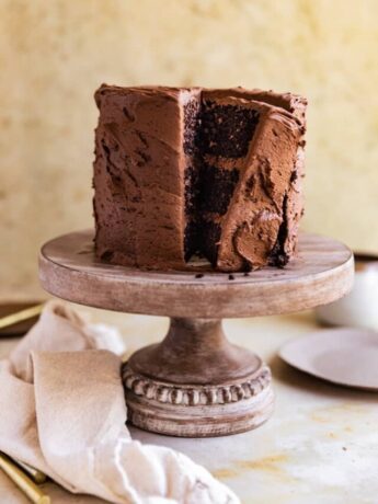 A chocolate cake with a slice cut out on an angle on a wooden cake stand.