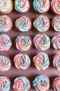 Multicolored cupcakes piped into rosettes on a pink tray.