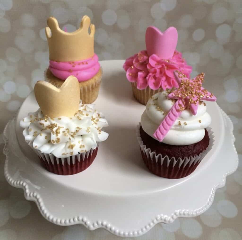 4 cupcakes with princess theme toppers on a cake stand.