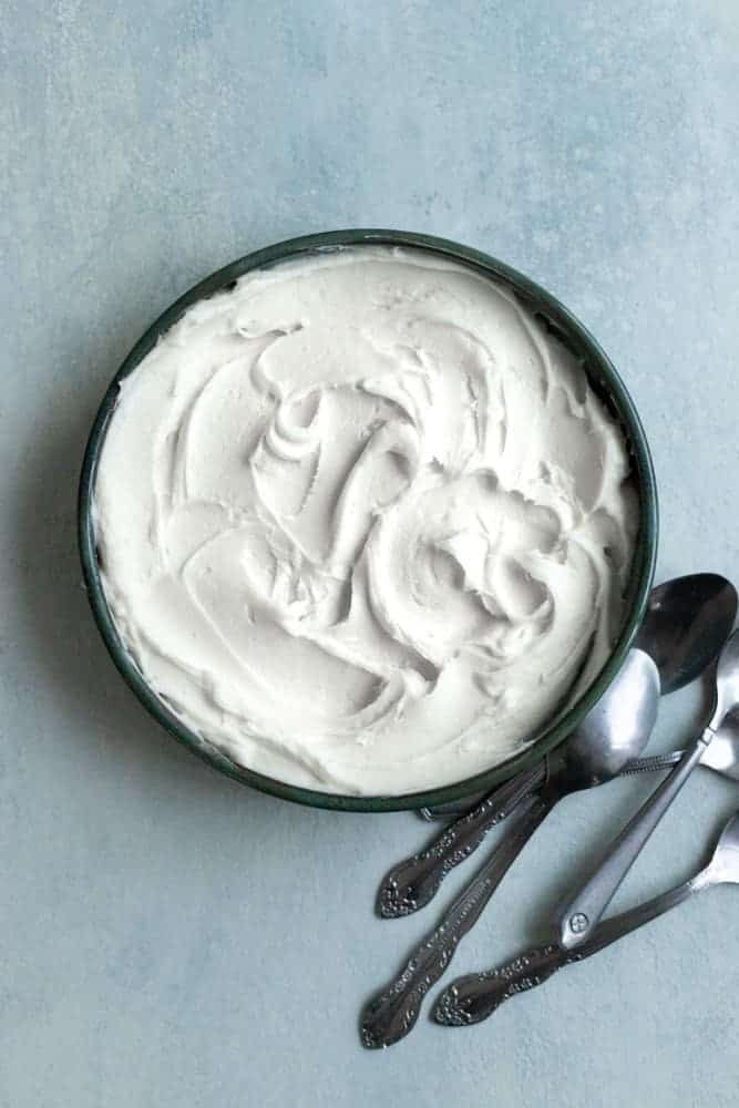 Thicken cream cheese frosting in a bowl on a blue surface.