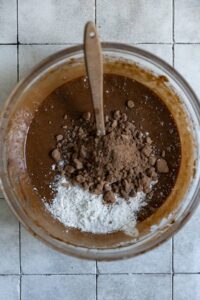 Dry ingredients added to brownie batter in a glass bowl.