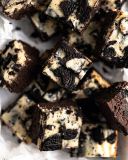 Oreo cheesecake brownies cut and layered on top of each other on parchment paper.