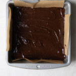 Brownie batter in a lined 8x8 square pan.