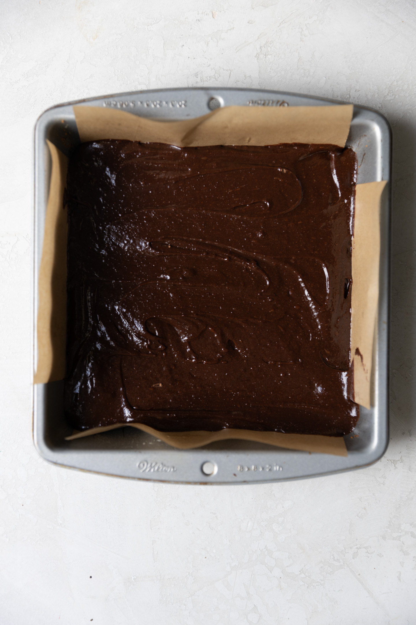 Brownie batter in a lined 8x8 square pan.