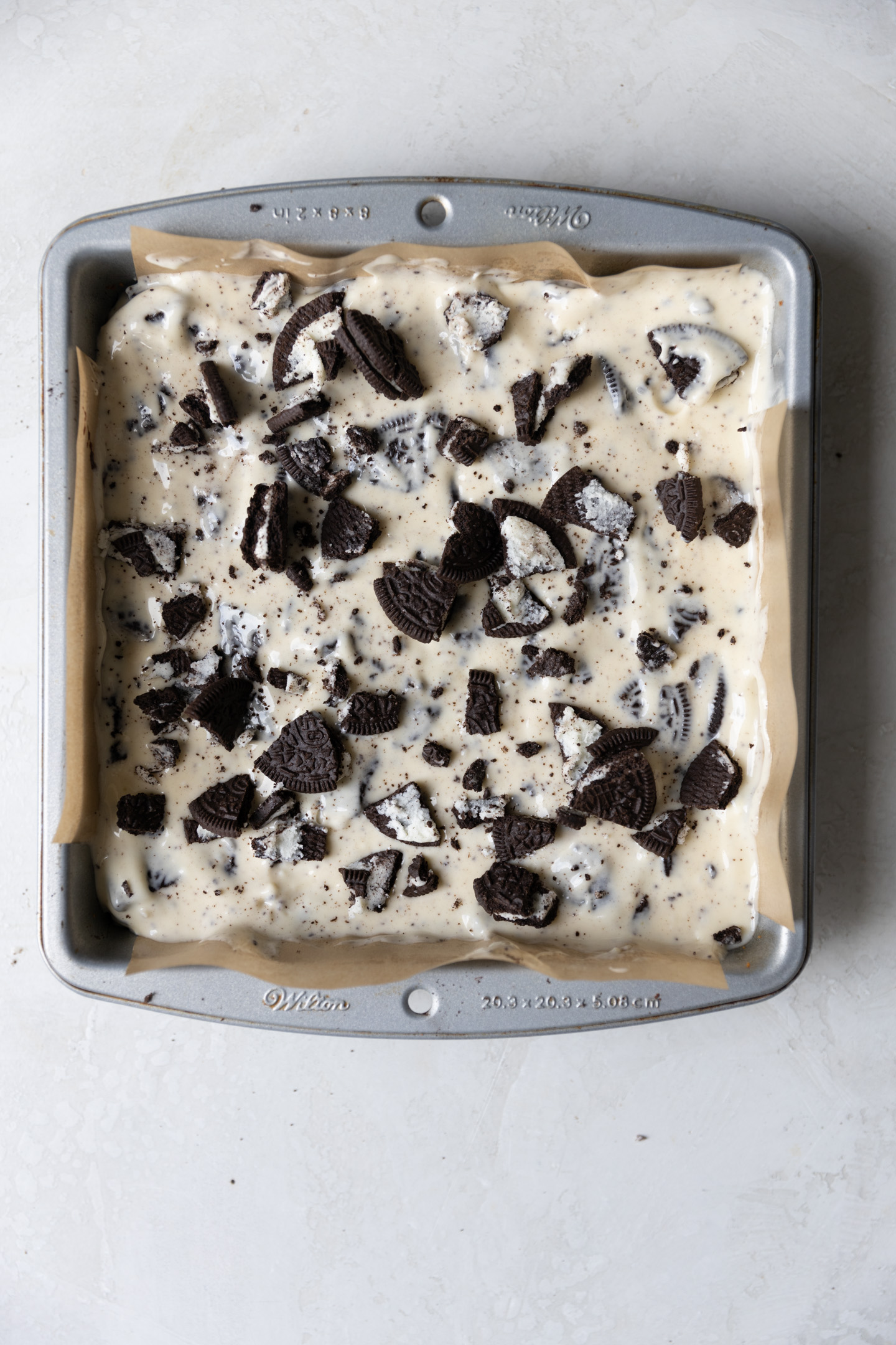 Oreo cheesecake batter topped with crushed Oreos in a brownie pan.