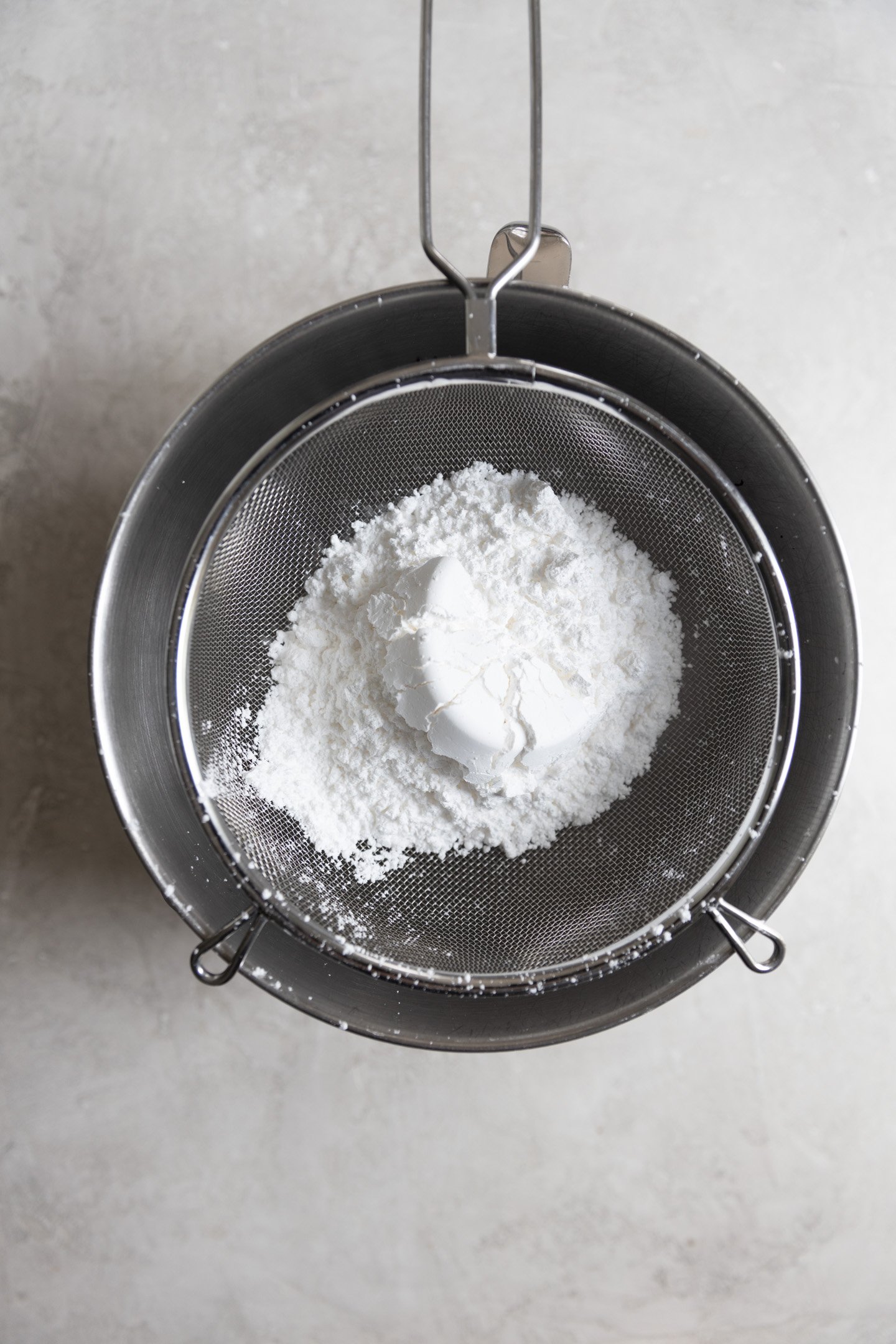 Powdered sugar in a sifter over a bowl.