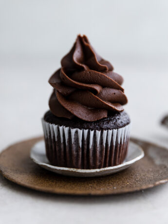 A chocolate cupcake with chocolate fudge frosting on small layered plates.