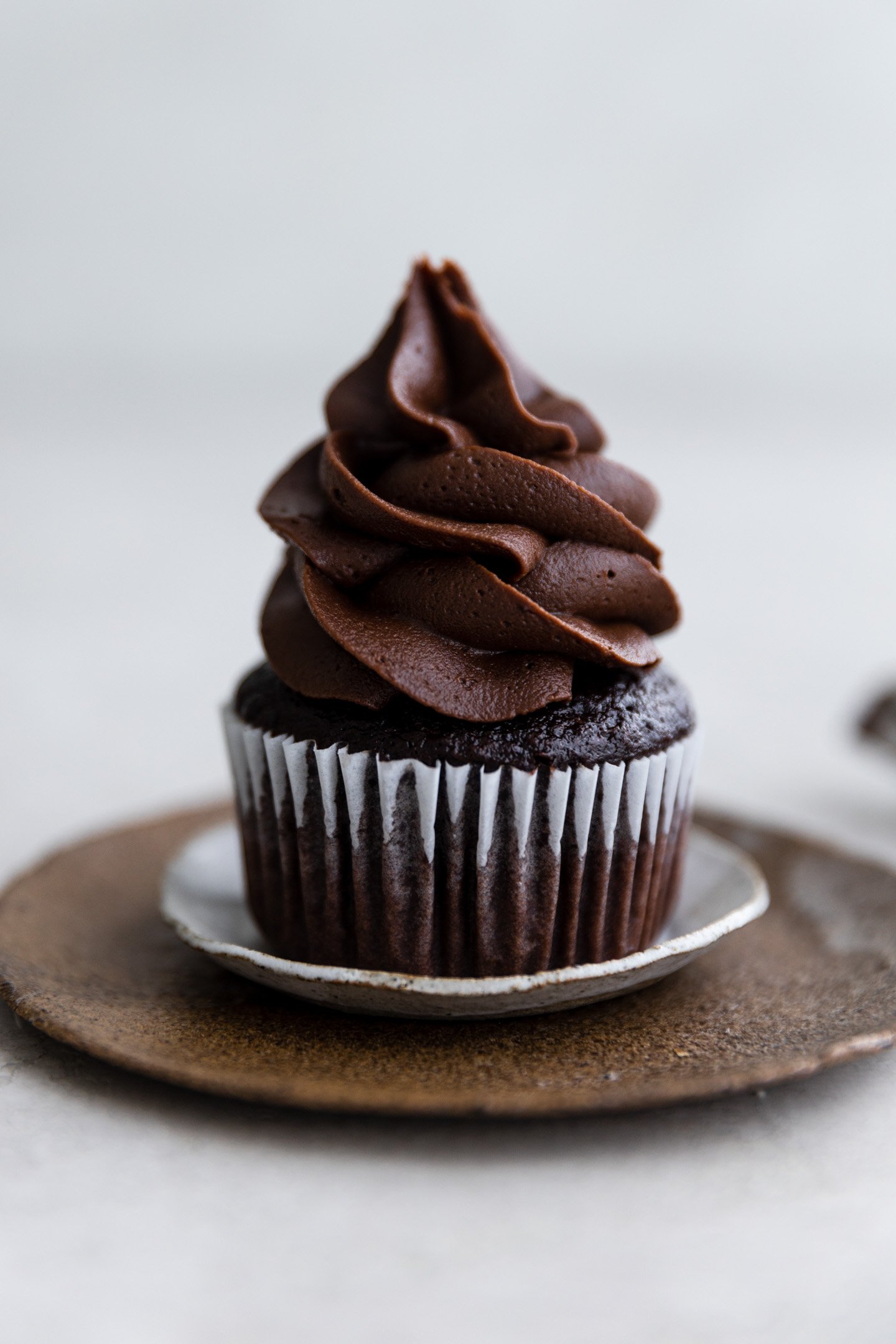 A chocolate cupcake with chocolate fudge frosting on small layered plates.