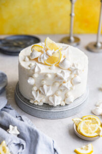 A lemon curd cake with white decorations on a gray surface next to a blue linen.