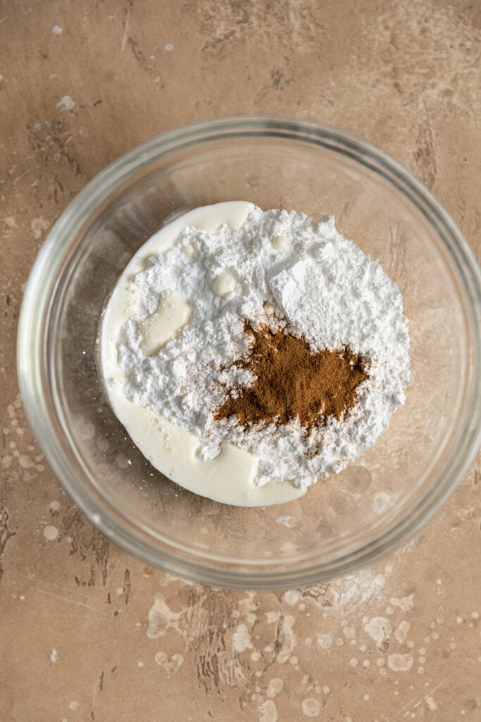 A glass bowl with powdered sugar, milk, and cinnamon inside.