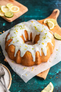 A 7 up bundt cake on a pieces of parchment paper and a wooden cutting board with lemon and lime slices next to it.