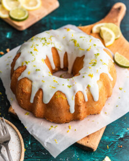 A 7 up bundt cake on a pieces of parchment paper and a wooden cutting board with lemon and lime slices next to it.
