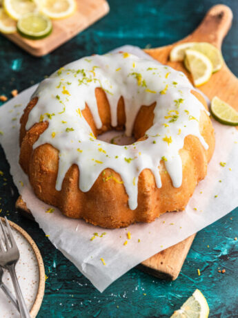 A 7 up bundt cake on a pieces of parchment paper and a wooden cutting board with lemon and lime slices next to it.