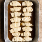 Unbaked apple dumplings in a sweet sauce in a 9x13 pan.