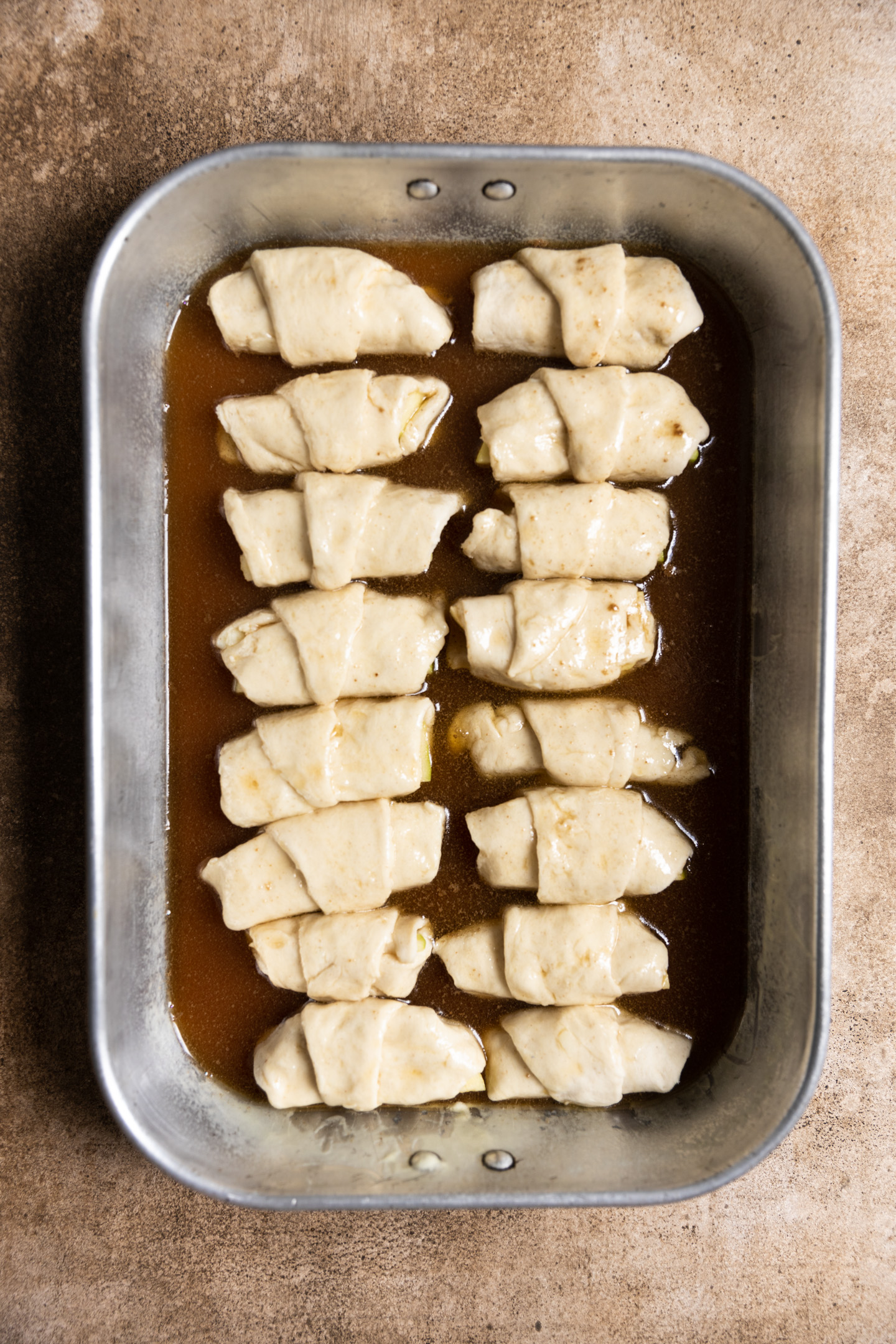 Unbaked apple dumplings in a sweet sauce in a 9x13 pan.