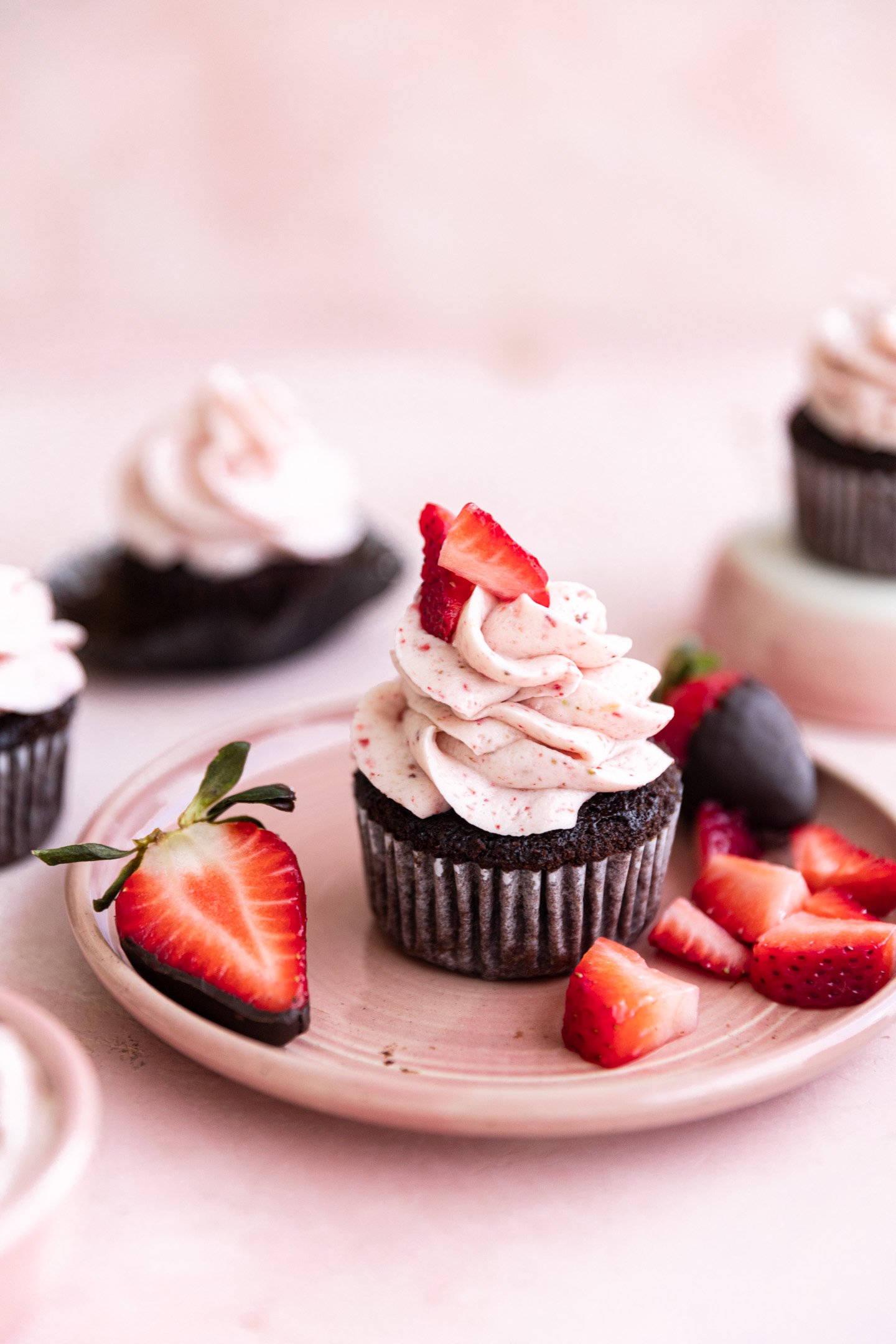 Chocolate strawberry cupcakes topped with fresh berries on a pink plate.