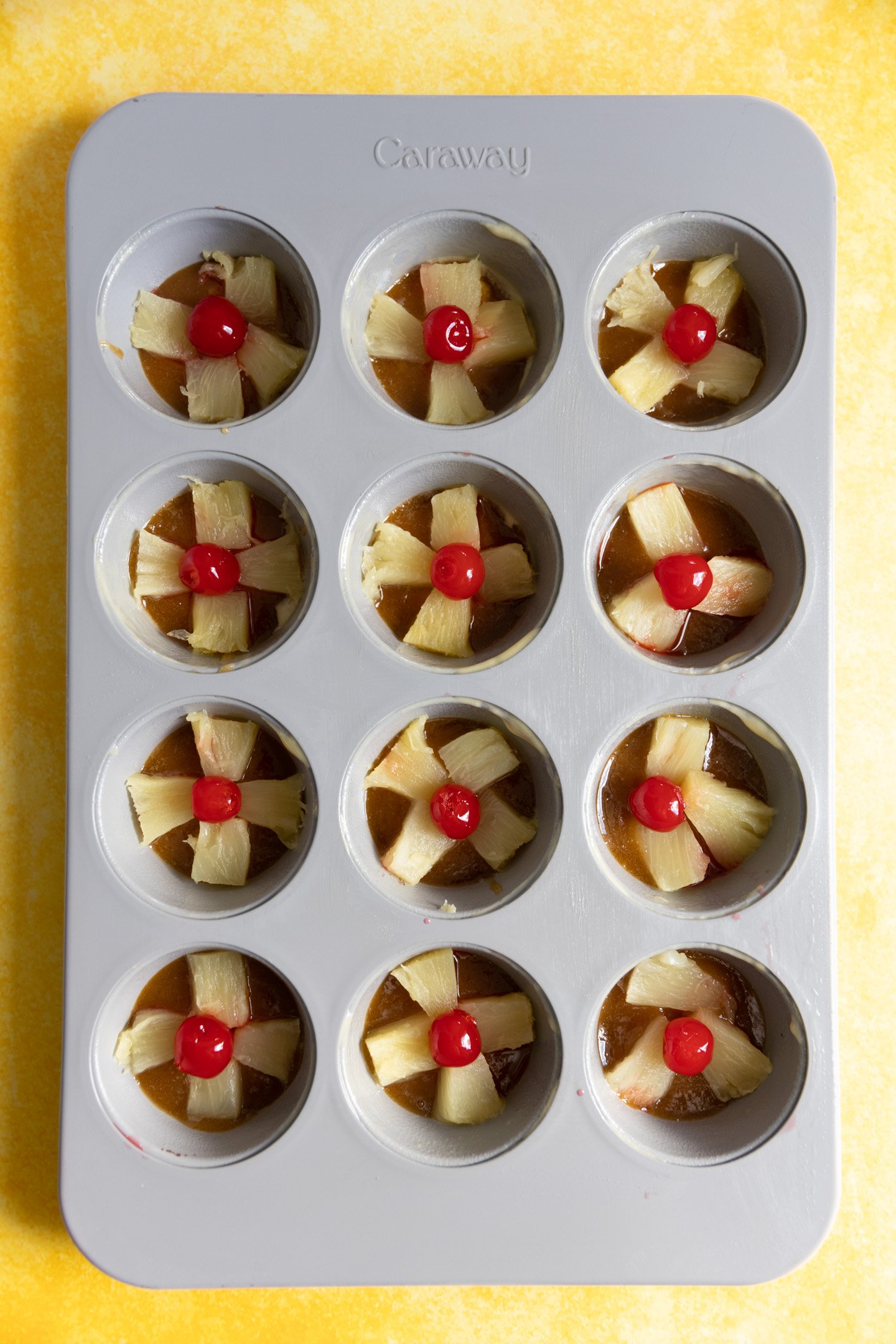 Pineapple pieces and cherries in the bottom of a muffin tin.