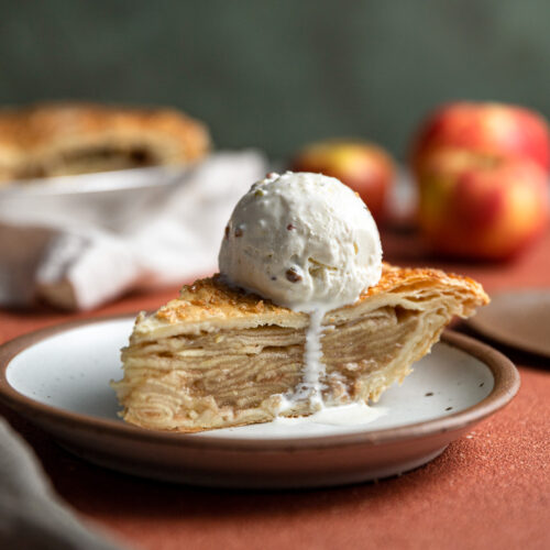 A slice of apple pie made with puff pastry with a scoop of ice cream on top.