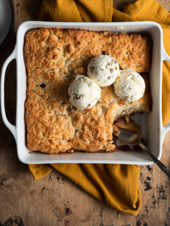 Apple cobbler with ice cream on top and a sliced scooped out with a spoon.
