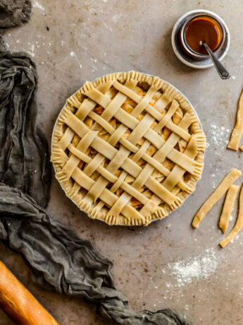 A pre baked apple pie with lattice crust on a beige surface.