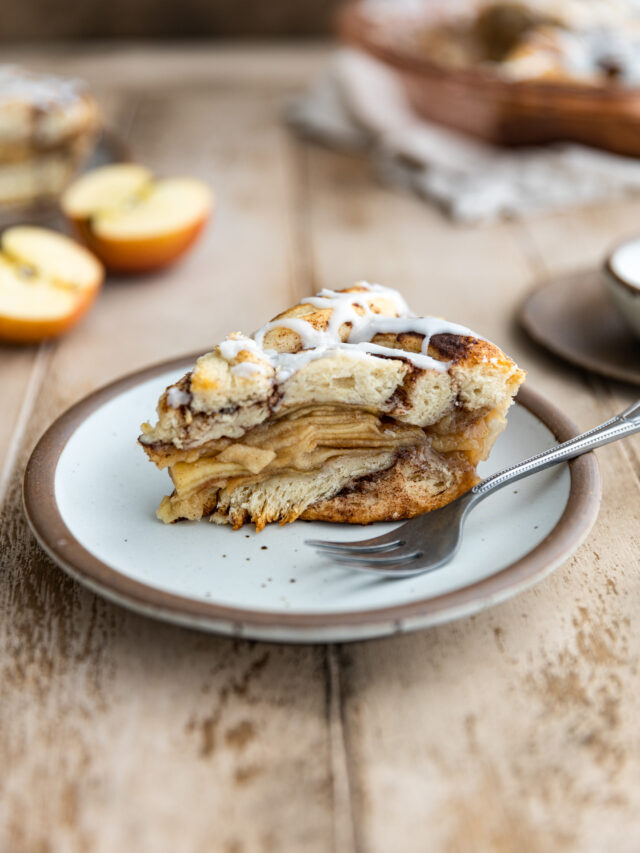 A slice of cinnamon roll apple pie on a plate with a fork.