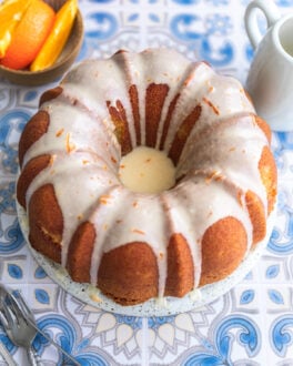 An orange bundt cake with icing on a blue patterend surface.