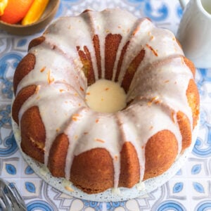 An orange bundt cake with icing on a blue patterend surface.