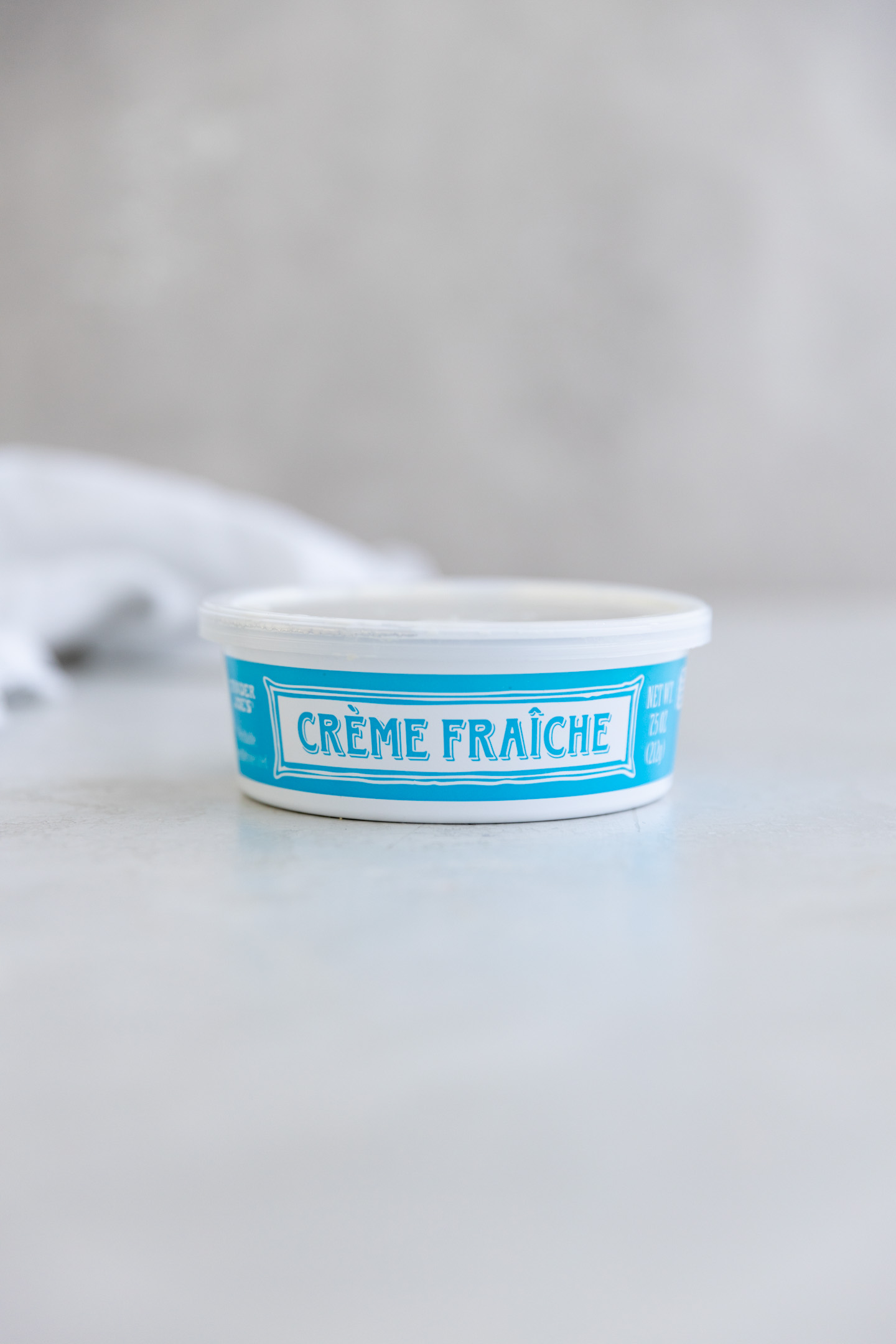 A tub of creme fraiche on a light grey surface.