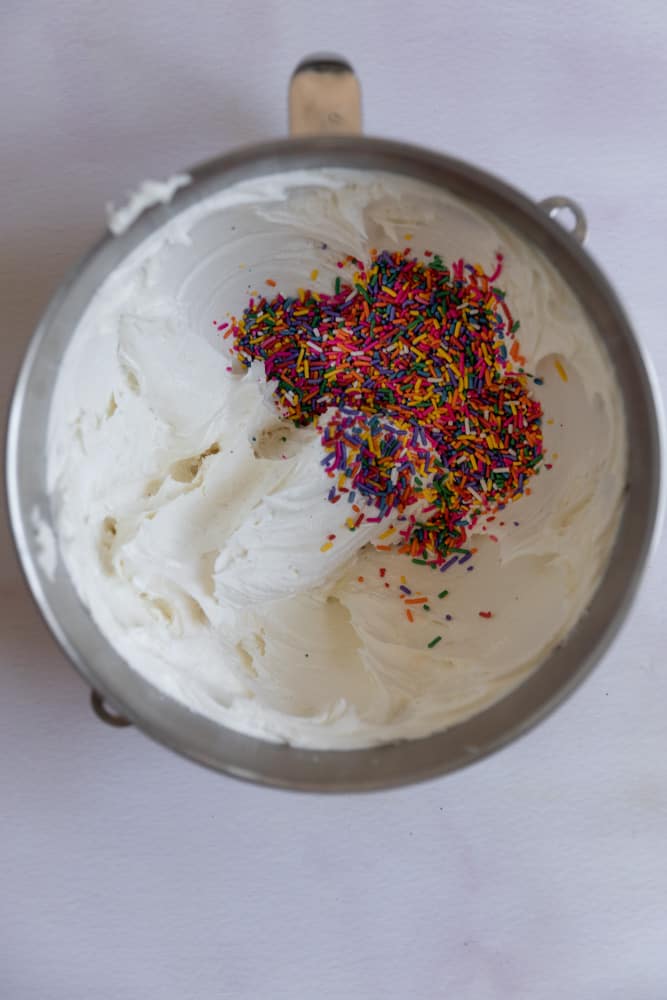 Sprinkles added to a bowl of white frosting.