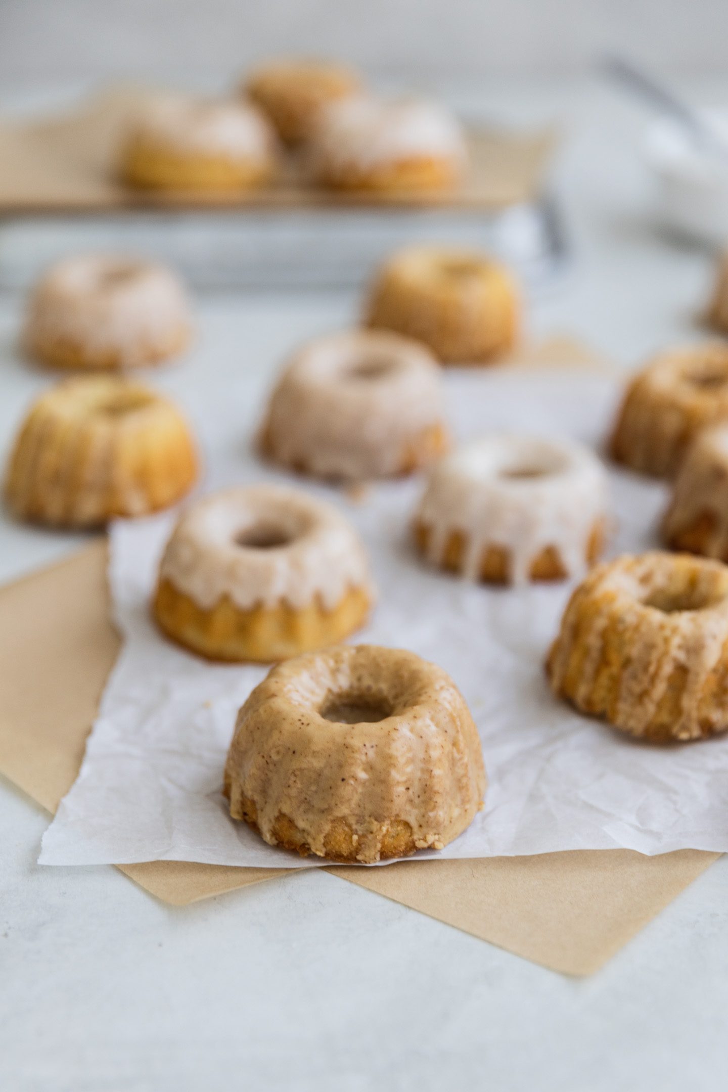 Mini iced bundt cakes on brown and white parchment paper.