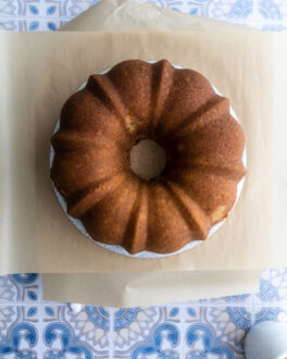 An orange bundt cake on a cake turner topped with parchment paper.