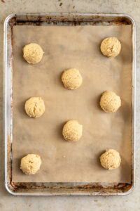 Cookie dough balls lined on a brown piece of parchment paper.