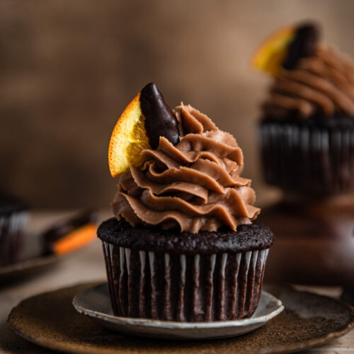 A chocolate cupcake topped with chocolate frosting and garnished with a chocolate covered orange slice.