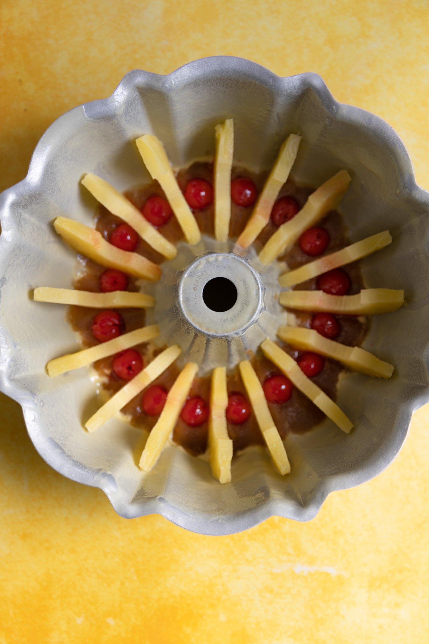 Pineapple slices and cherries lined in a bundt pan.