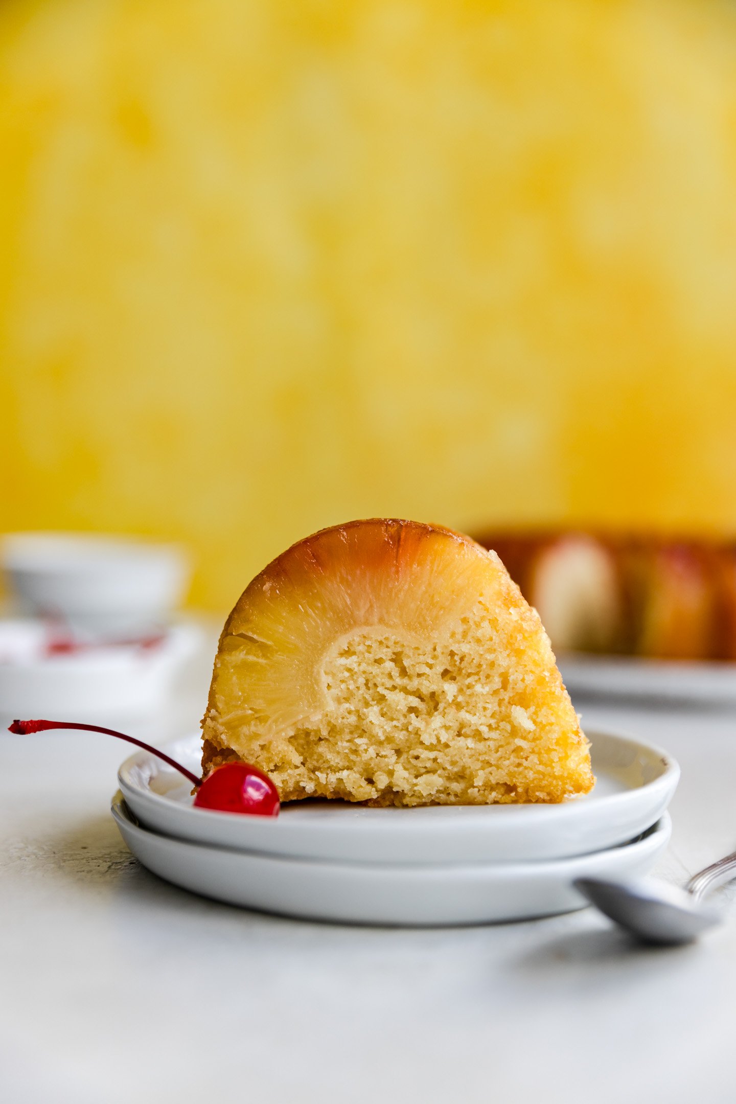 A slice of a pineapple upside down bundt cake on a stack of white plates.
