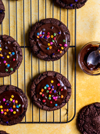 Cosmic brownie cookies on a wire rack next to a small bowl of melted chocolate.
