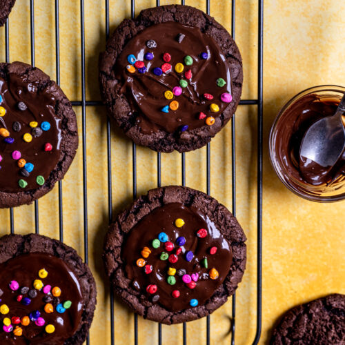 Cosmic brownie cookies on a wire rack next to a small bowl of melted chocolate.