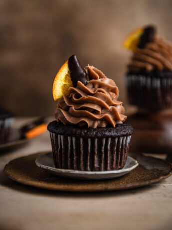 A chocolate cupcake topped with chocolate frosting and garnished with a chocolate covered orange slice.
