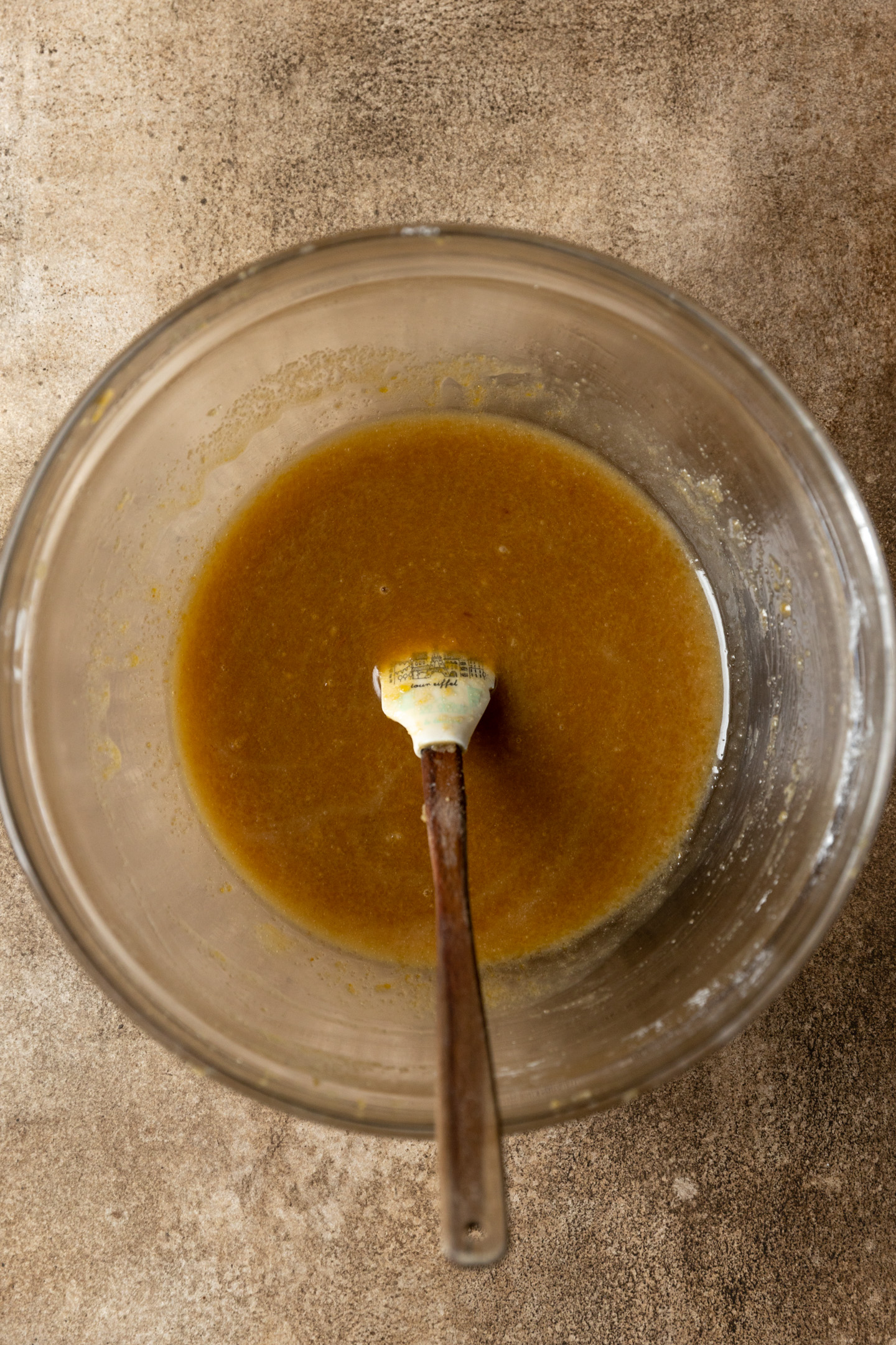 Melted butter, brown sugar, and white sugar stirred in a glass mixing bowl.