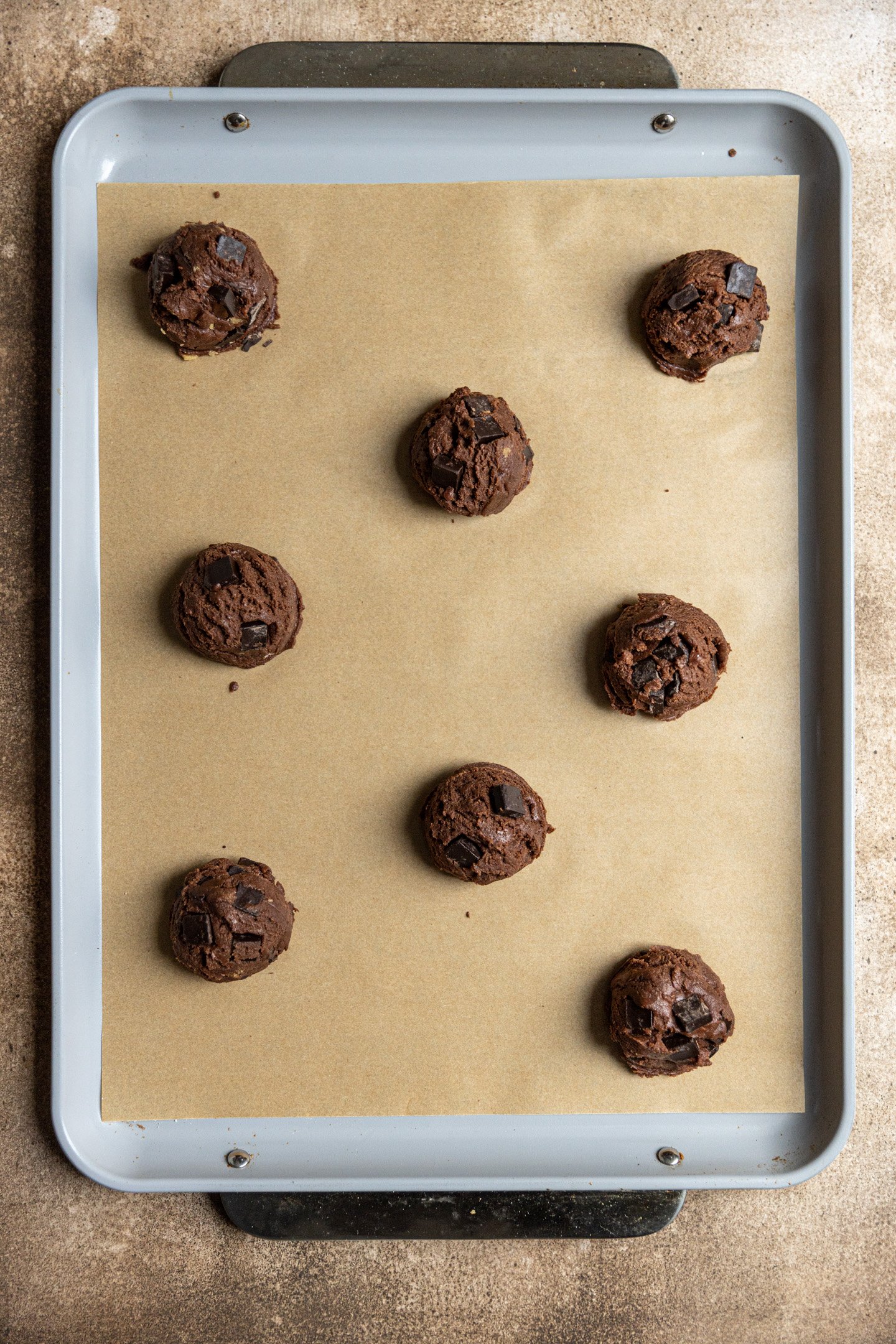 Double chocolate chip cookie dough balls on a parchment line sheet tray.