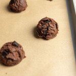 A chocolate cookie dough ball on a cookie sheet lined with brown parchment paper.