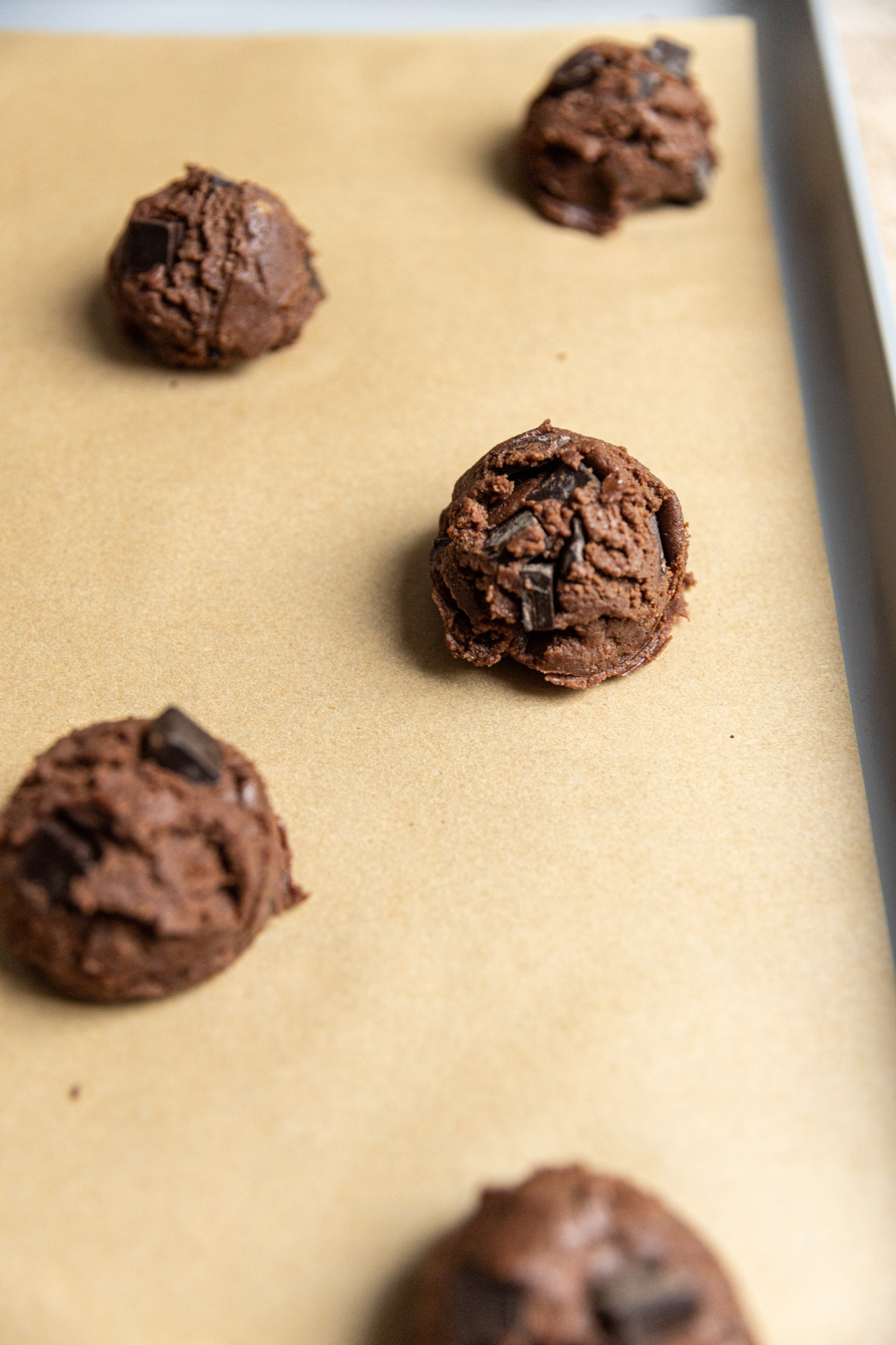 A chocolate cookie dough ball on a cookie sheet lined with brown parchment paper.
