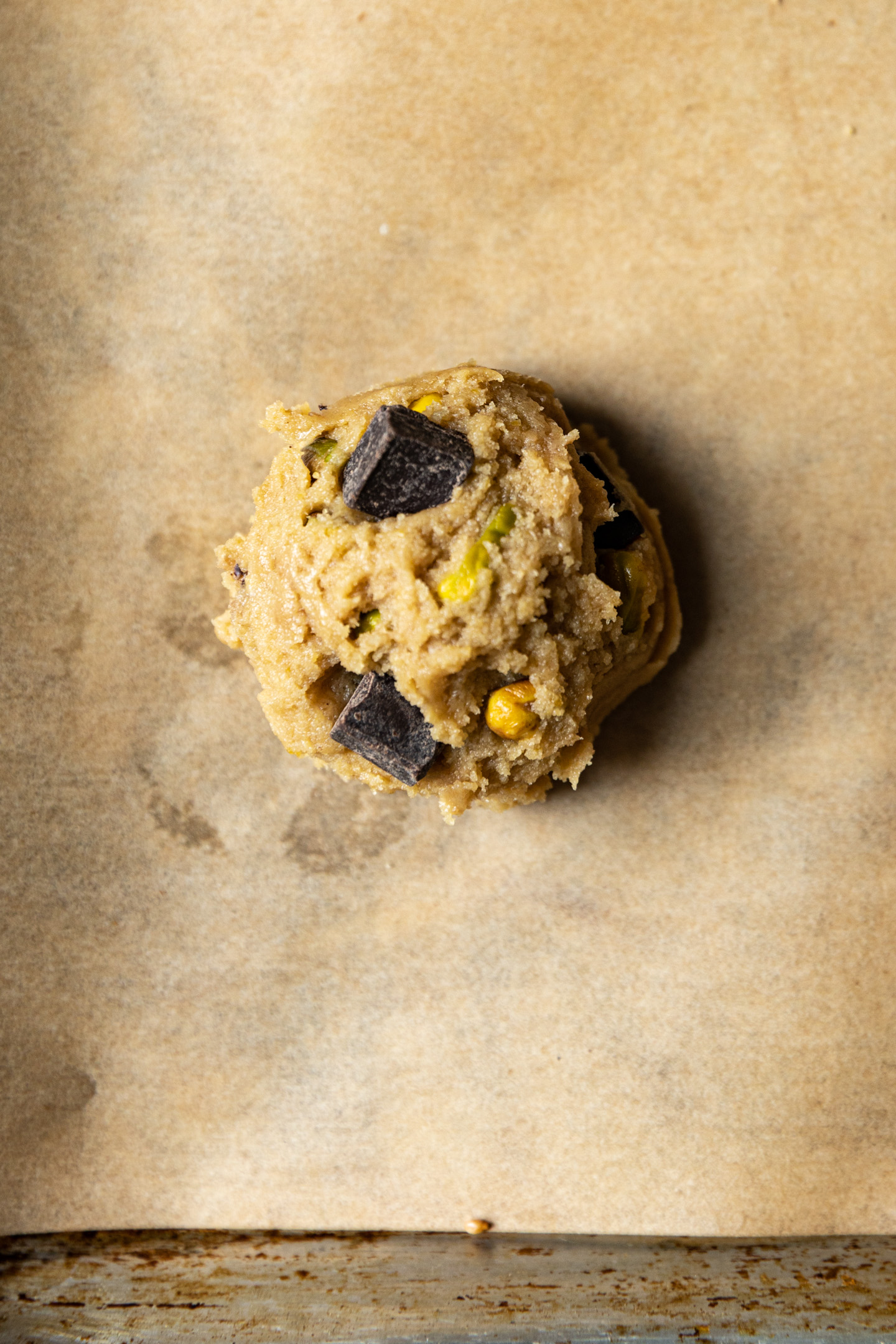 Pistachio and chocolate cookie dough ball on parchment paper.