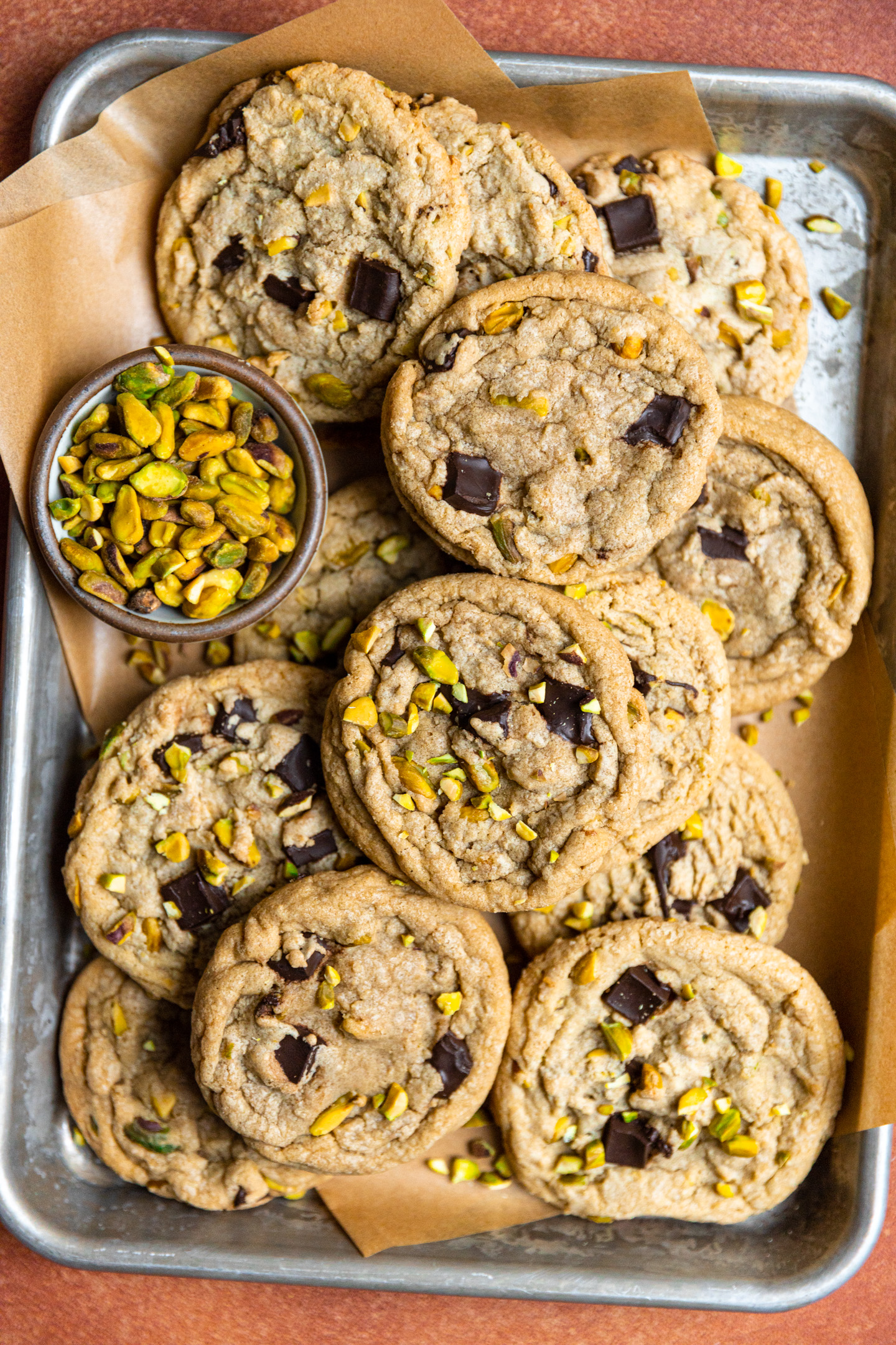 Pistachio chocolate chip cookies on a parchment lined tray next to a bowl of pistachios.